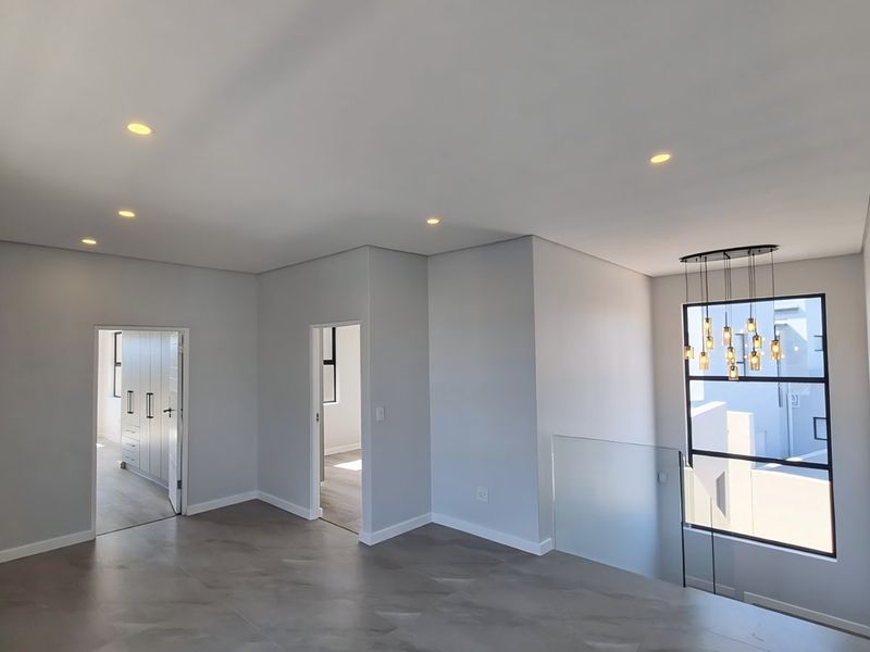 A bright and modern landing area featuring large windows, glass balustrades, and neutral tiled flooring, providing a clean and contemporary transition space.