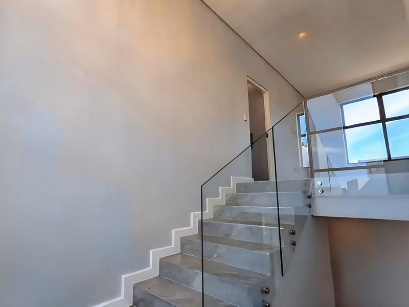Modern hallway featuring a sleek staircase with a frameless glass balustrade, large window for natural light, and clean, minimalist finishes.