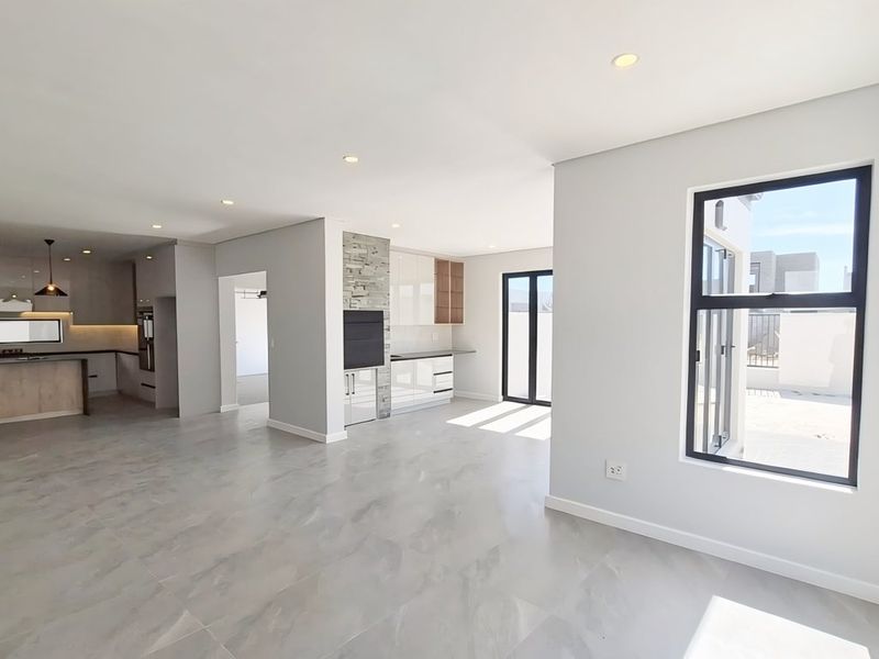 Spacious open-plan living and kitchen area featuring modern cabinetry, a central island, stone feature wall, and large windows providing ample natural light.