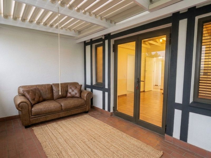 A covered patio area featuring terracotta tile flooring, a louvre roof system, and modern aluminium-framed glass doors providing access to the interior.
