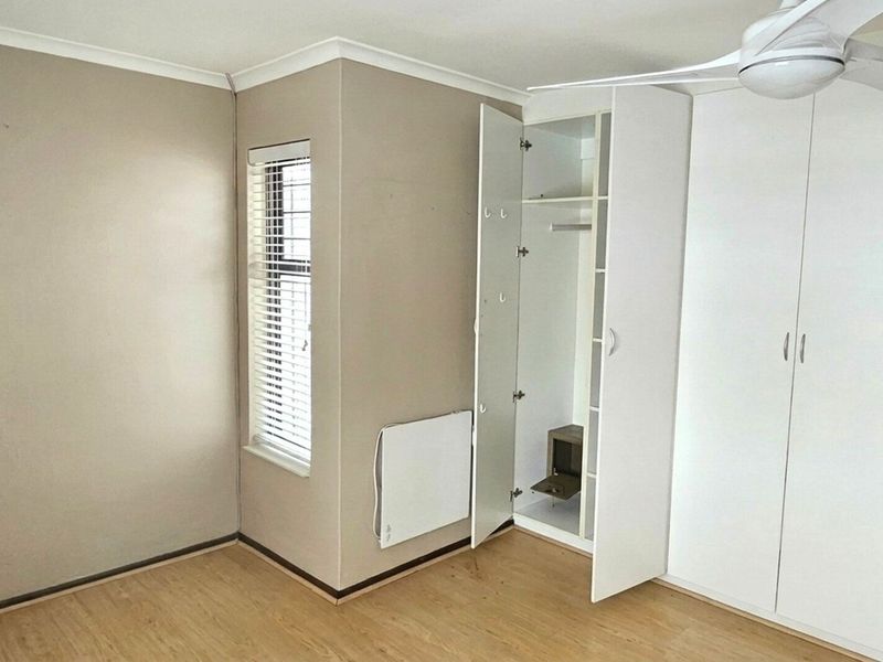 A clean, empty bedroom featuring built-in cupboards, a ceiling fan, laminate flooring, and a wall-mounted heater, offering a neutral canvas for personalization.
