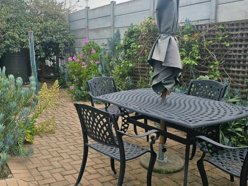 A private rear garden area featuring brick paving, established perimeter landscaping, a precast concrete boundary wall, and a water storage tank.