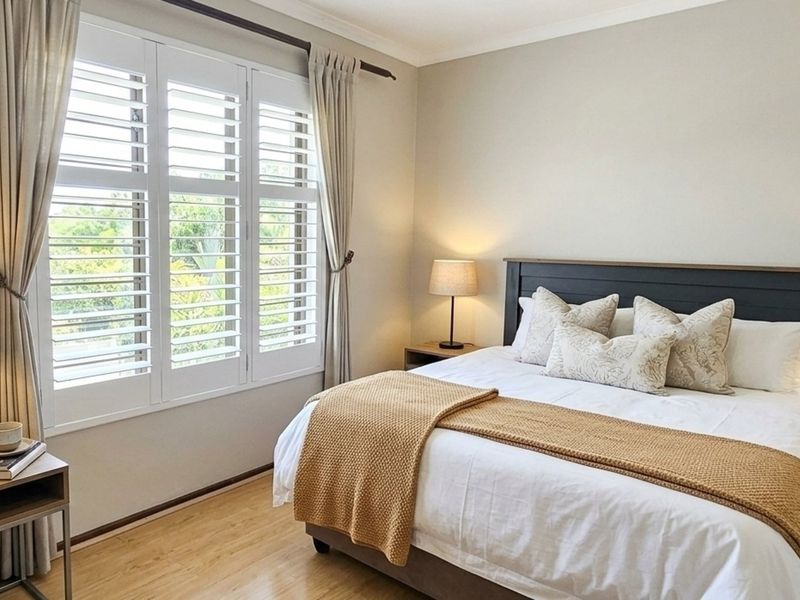 A well-maintained bedroom featuring light laminate flooring, neutral walls, and white plantation shutters that provide natural light and privacy.