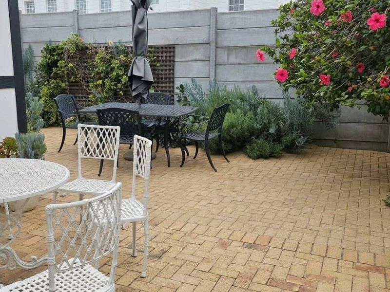 A paved outdoor patio area featuring a precast concrete boundary wall and established garden landscaping.