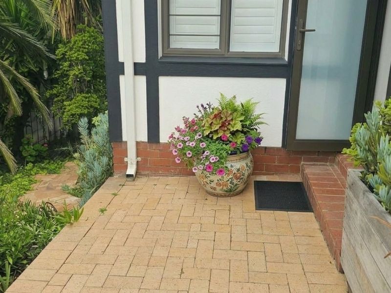 A paved patio area featuring brick foundation detailing, a downpipe, and access to the home through a glass door and window.