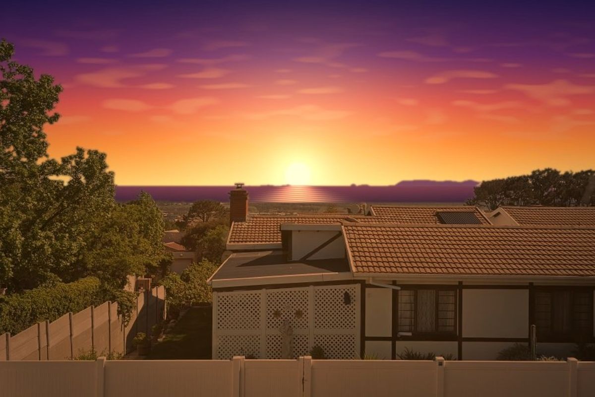 Rear view of the property featuring a tiled roof, chimney, and solar panel, set against a scenic sunset backdrop.