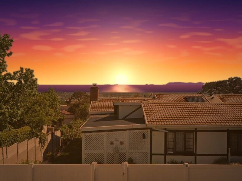 Rear view of the property featuring a tiled roof, chimney, and solar panel, set against a scenic sunset backdrop.