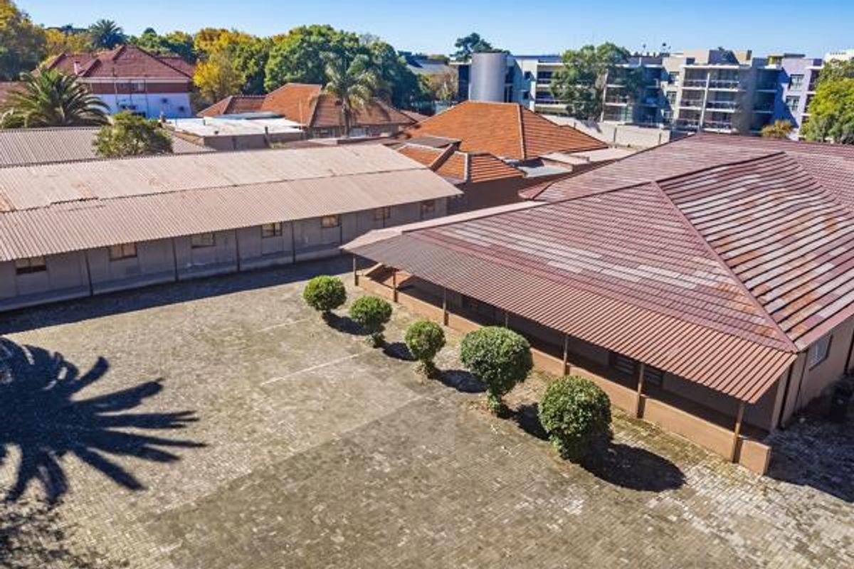 Aerial view of a commercial property complex featuring multiple buildings with tiled roofs, a paved parking area, and established landscaping.