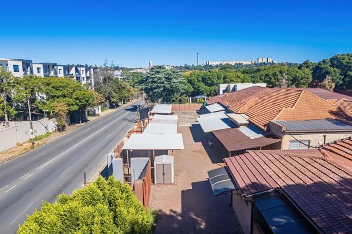 Aerial view of the commercial property showing tiled roof structures, paved parking area with carports, and proximity to the main road.