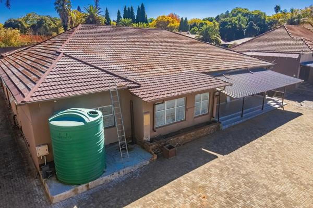Aerial view of the rear exterior featuring a tiled roof, a large water storage tank, and a covered patio area with paved surroundings.