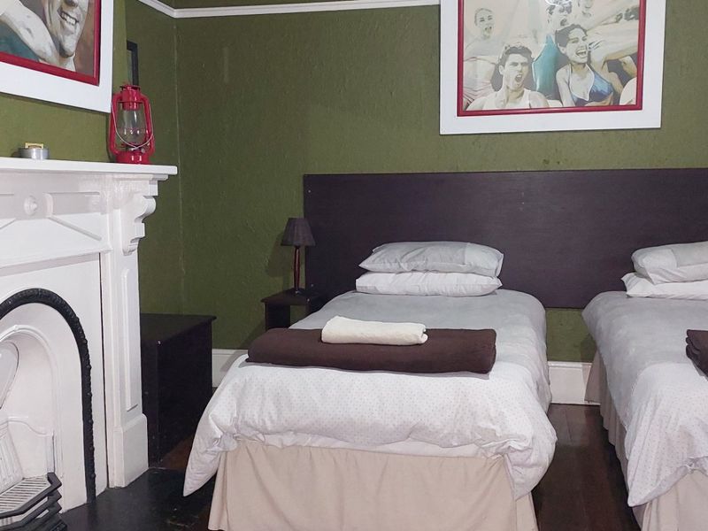 A bedroom featuring a traditional fireplace with a white mantelpiece, dark timber flooring, and green painted walls.