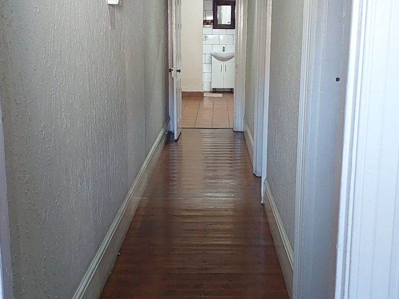 A long hallway featuring original timber flooring, a decorative archway, and a classic pendant light, leading towards a bathroom area.
