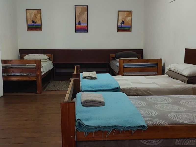 A spacious bedroom featuring timber flooring and a built-in headboard, currently configured with multiple beds.