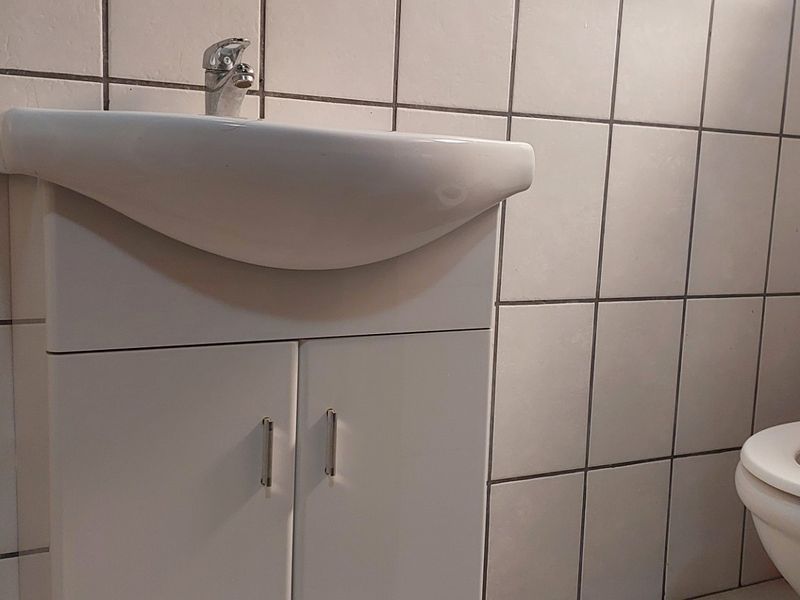 A functional bathroom featuring a white vanity cabinet with a ceramic basin and a standard toilet, finished with full-height wall tiling.