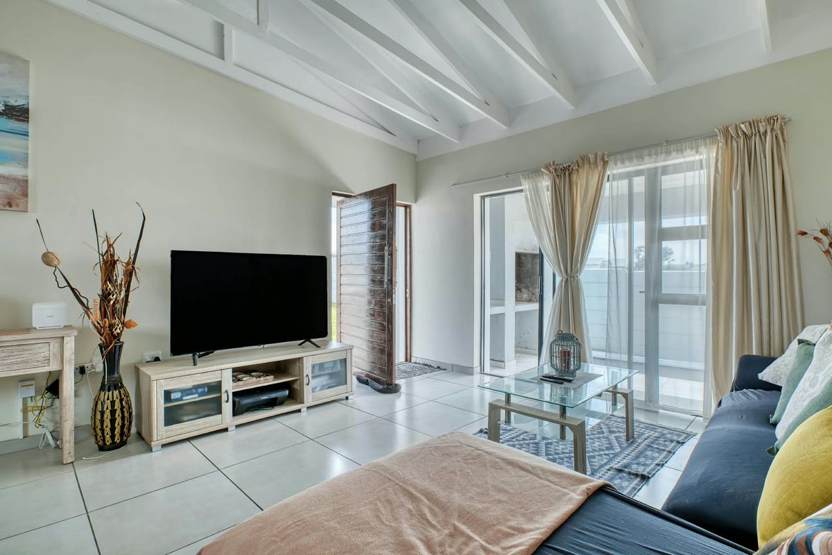 Bright living room featuring exposed white timber beams, large format floor tiles, and sliding glass doors providing access to an outdoor patio area.