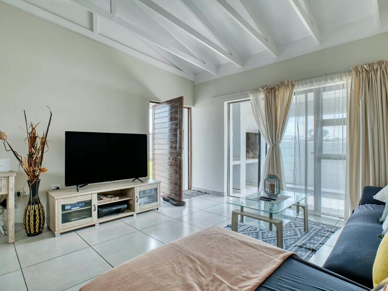 Bright living room featuring exposed white timber beams, large format floor tiles, and sliding glass doors providing access to an outdoor patio area.