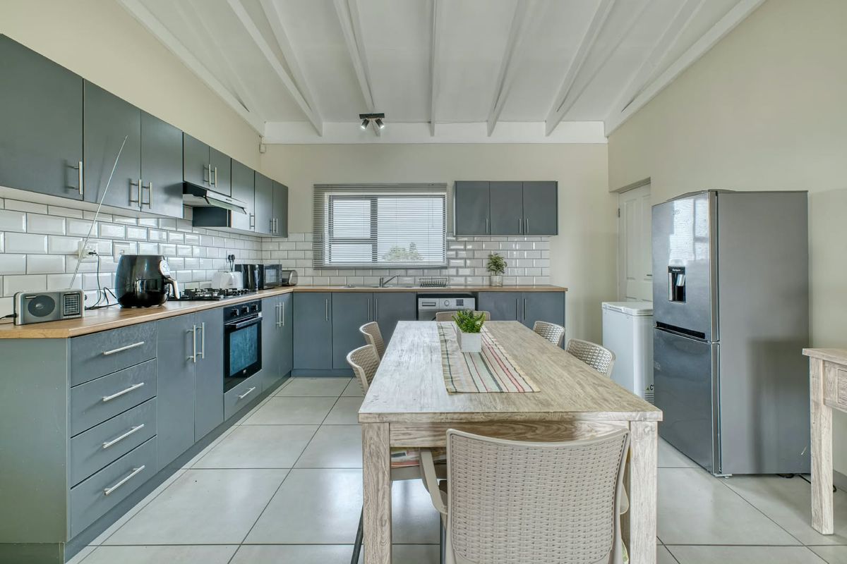 Modern kitchen featuring grey cabinetry, subway tile backsplash, integrated oven, gas hob, and exposed beam ceilings with tiled flooring throughout.
