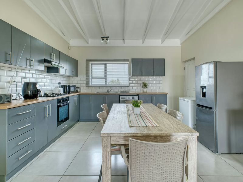 Modern kitchen featuring grey cabinetry, subway tile backsplash, integrated oven, gas hob, and exposed beam ceilings with tiled flooring throughout.