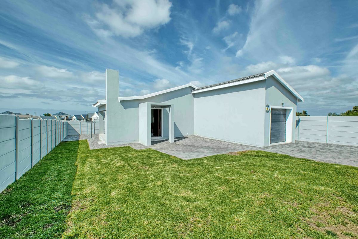 Rear view of the property featuring a paved patio area, a single garage, and a well-maintained lawn enclosed by precast boundary walls.
