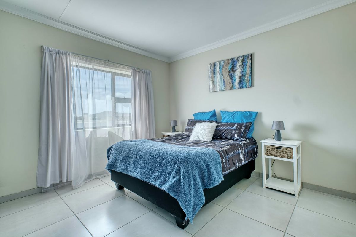 A bright and well-maintained bedroom featuring neutral tiled flooring, crisp cornicing, and a large window allowing for ample natural light.