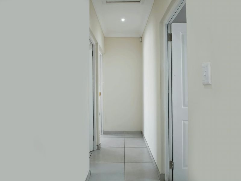 A clean, neutral hallway featuring tiled flooring and recessed downlighting, providing access to multiple rooms within the property.