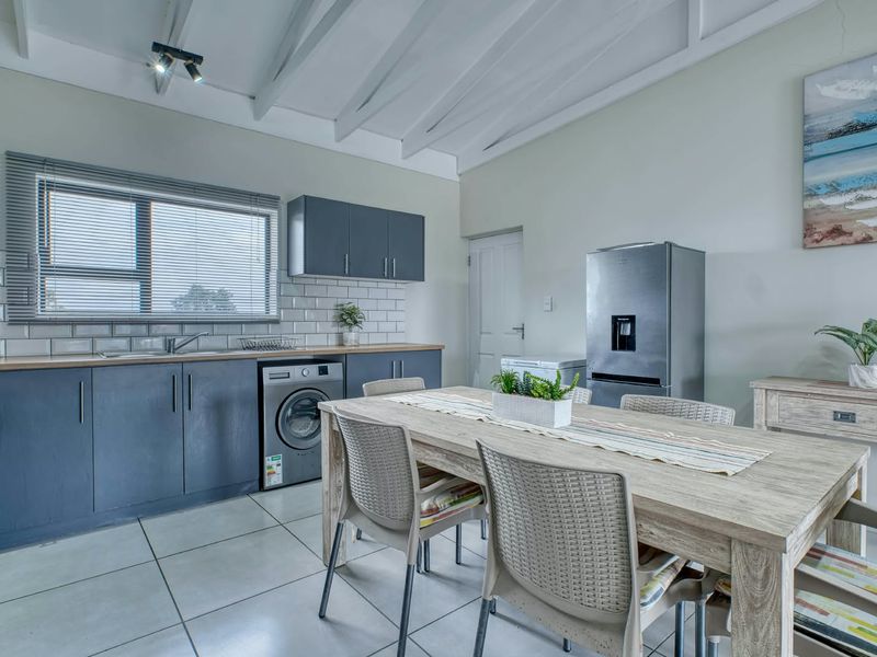 Open-plan kitchen and dining area featuring modern dark cabinetry, subway tile backsplash, timber countertops, and exposed beam ceilings with tiled flooring throughout.
