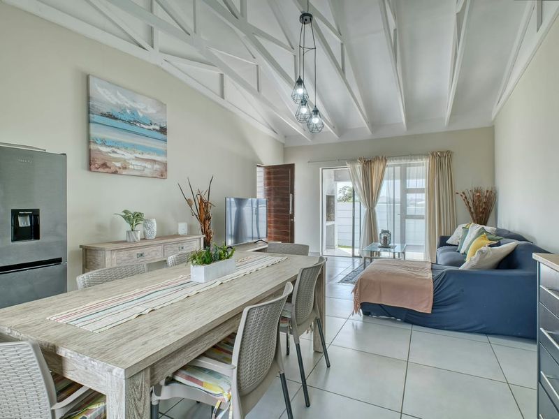 Spacious open-plan living and dining area featuring high vaulted ceilings with exposed rafters, tiled flooring, and direct access to an outdoor patio.