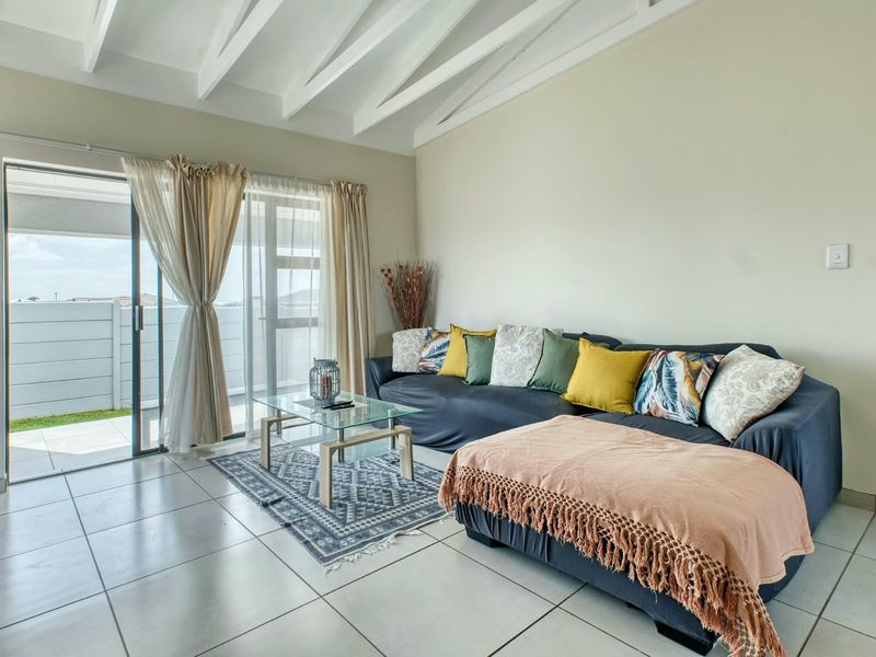 Bright living room featuring exposed white ceiling beams, neutral tiled flooring, and a large sliding glass door providing access to the outdoor patio area.