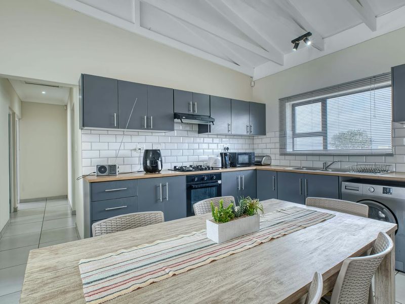 Modern open-plan kitchen featuring dark grey cabinetry, subway tile backsplash, wooden countertops, and exposed white timber rafters, seamlessly integrated with the dining area.