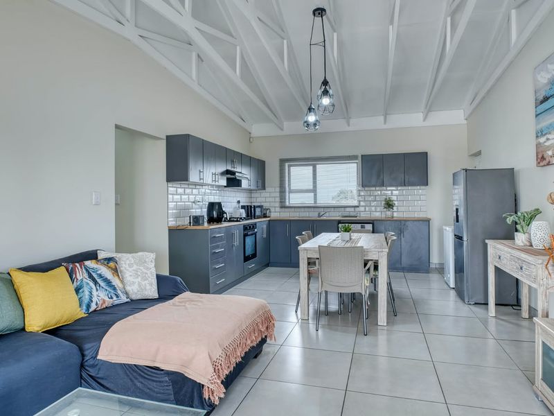 Spacious open-plan kitchen and living area featuring vaulted ceilings with exposed beams, modern grey cabinetry, subway tile backsplash, and neutral ceramic floor tiles.
