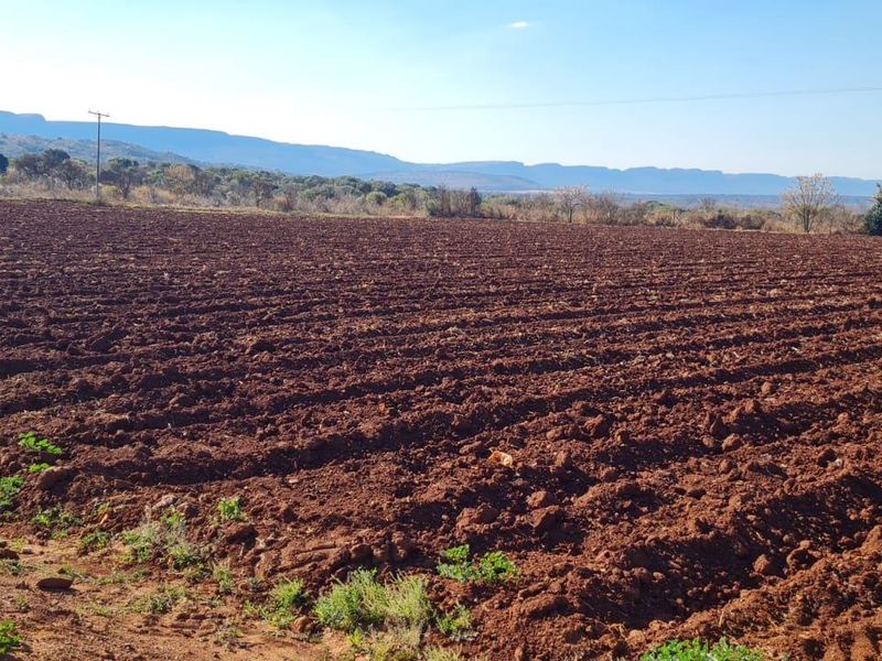 Expansive view of tilled agricultural land set against a scenic mountain backdrop, ideal for farming or rural development.