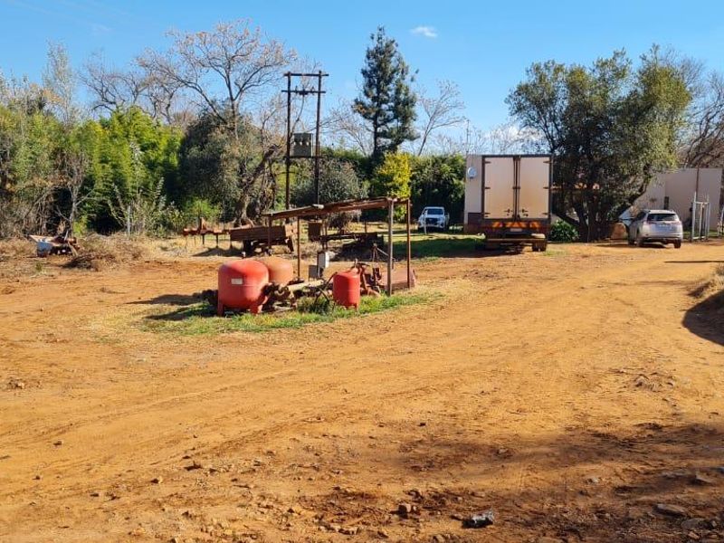 A wide view of the farm grounds featuring an unpaved driveway, electrical infrastructure, and water storage facilities on the property.