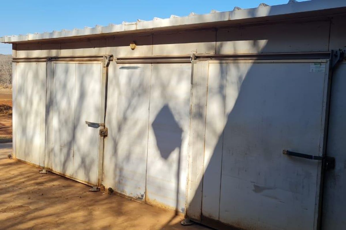A functional utility storage structure featuring metal sliding doors and a corrugated roof, situated on a farm property.