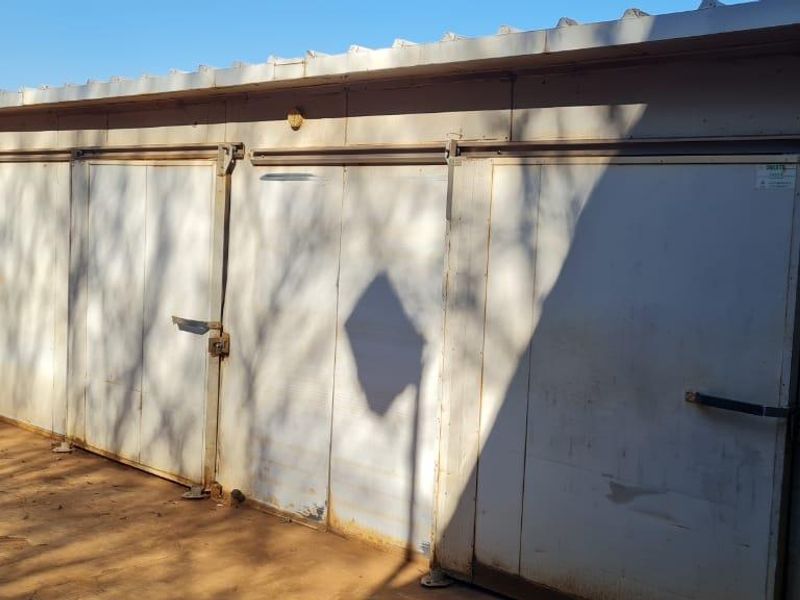 A functional utility storage structure featuring metal sliding doors and a corrugated roof, situated on a farm property.