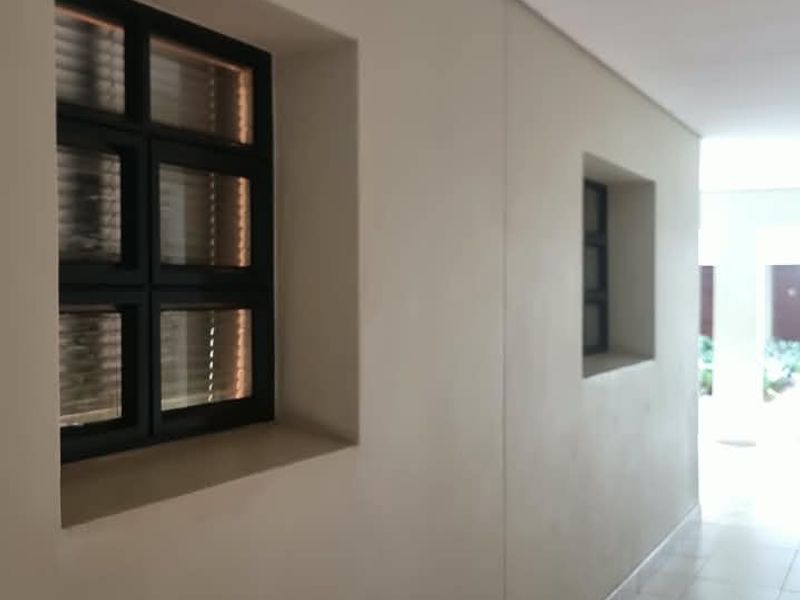 A clean, well-lit hallway featuring neutral walls, tiled flooring, and recessed downlights with black-framed windows providing natural light.