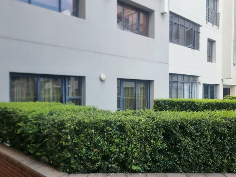 Exterior view of the apartment building featuring manicured hedging, a brick retaining wall, and modern aluminium window and door frames.