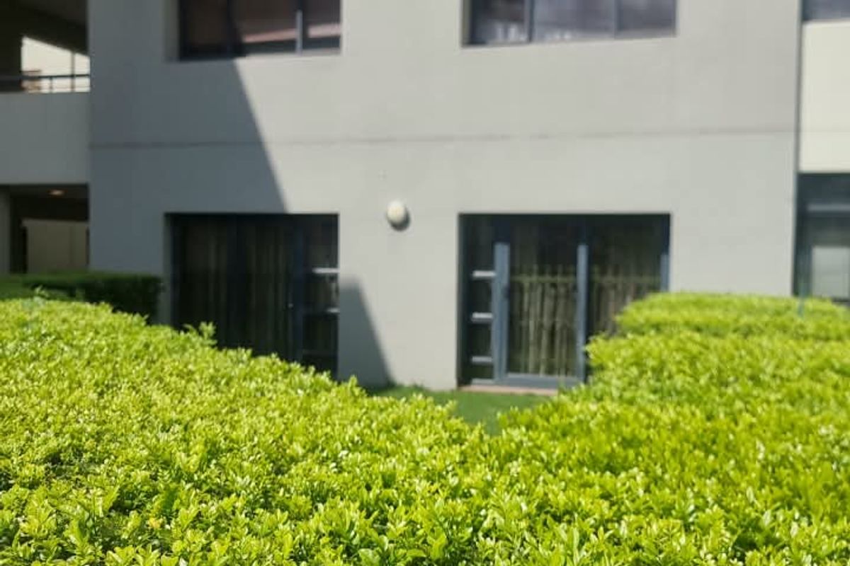A view of the apartment building exterior featuring modern grey facade, balcony railings, and sliding glass doors overlooking a landscaped garden area.