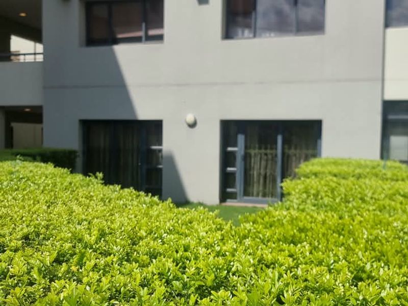 A view of the apartment building exterior featuring modern grey facade, balcony railings, and sliding glass doors overlooking a landscaped garden area.