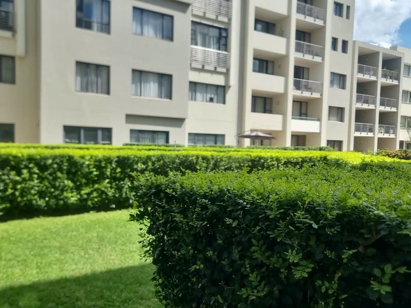 A view of the apartment complex exterior featuring well-maintained green hedges, landscaped lawn areas, and multi-story residential balconies.