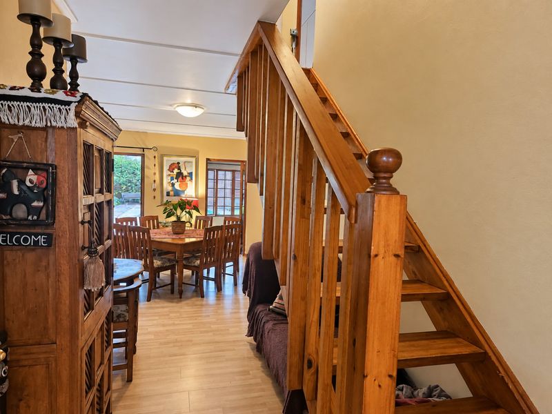 Open plan living and dining area featuring a prominent wooden staircase with balustrade and light-toned laminate flooring.