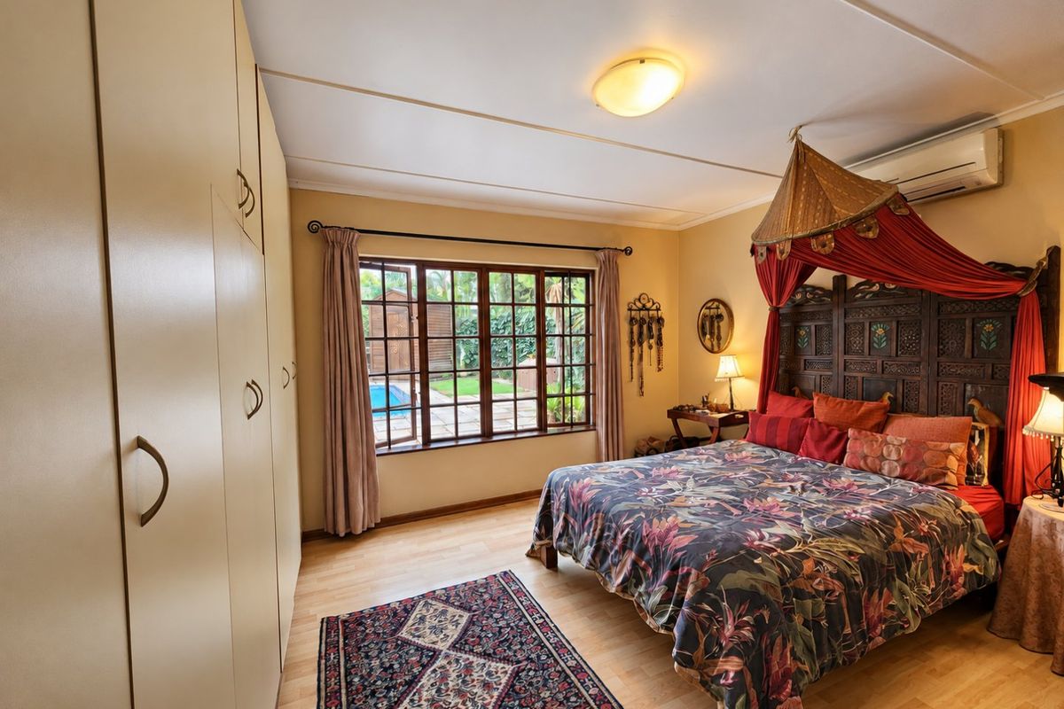 Spacious bedroom featuring built-in cupboards, laminate flooring, and a split-system air conditioner, with direct views overlooking the garden and pool area.