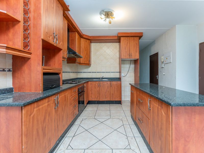 A functional kitchen featuring wood-look cabinetry, granite countertops, built-in oven, hob, and a breakfast bar, offering a practical layout for daily meal preparation.