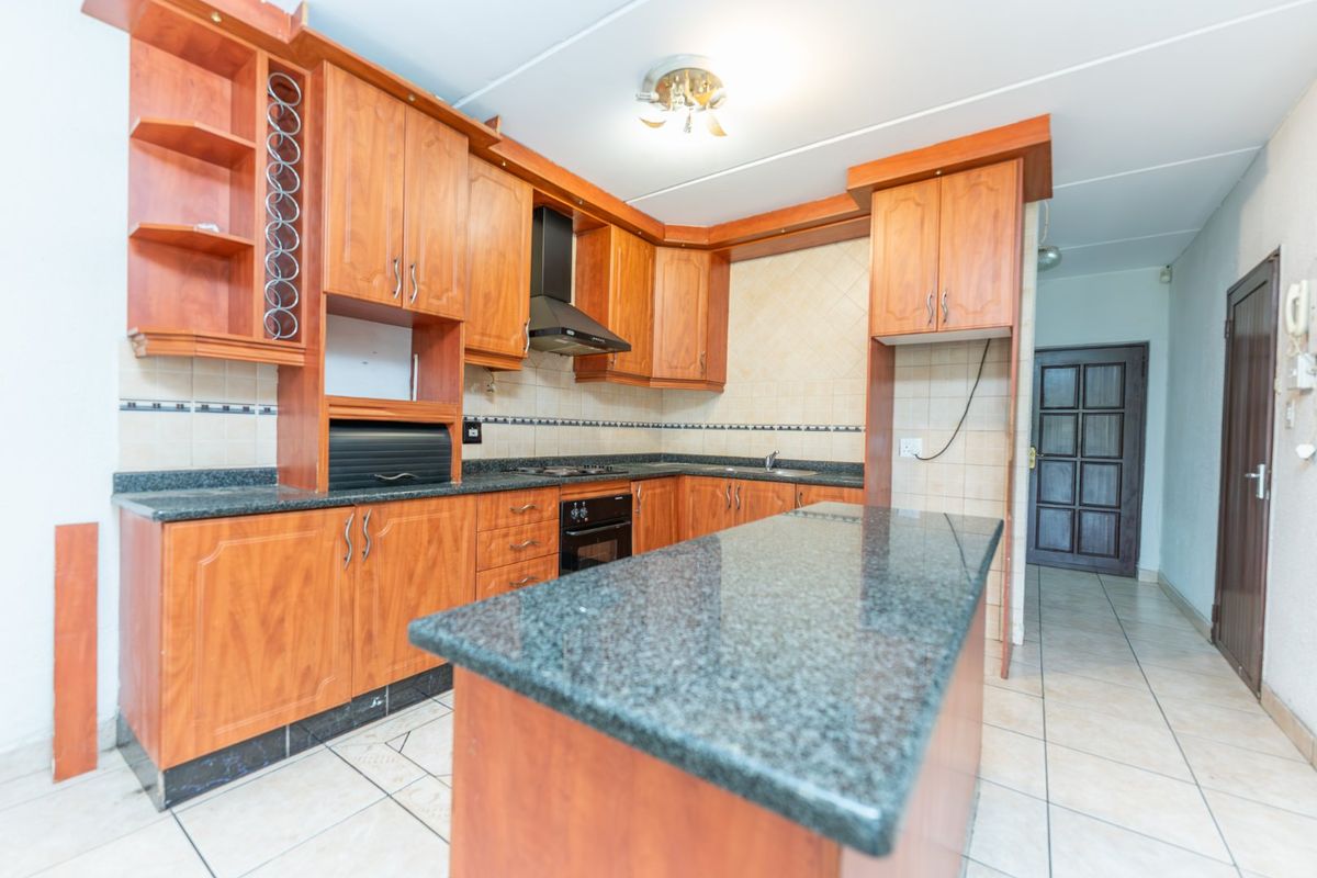 A functional kitchen featuring wooden cabinetry, granite countertops, built-in oven, and hob, with a central island and tiled flooring throughout.