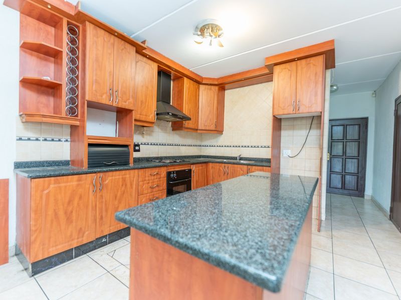A functional kitchen featuring wooden cabinetry, granite countertops, built-in oven, and hob, with a central island and tiled flooring throughout.