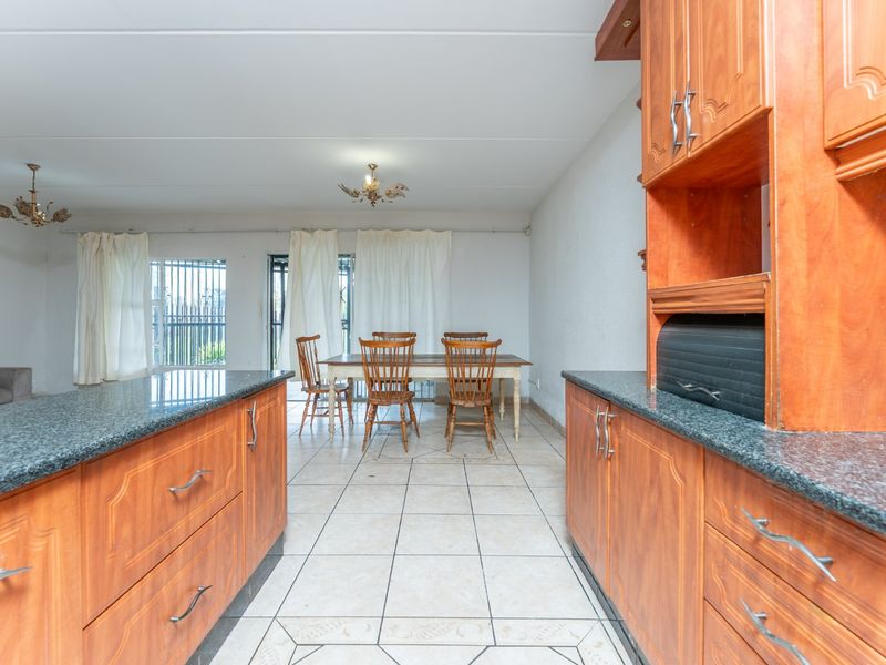 Open-plan kitchen and dining area featuring wooden cabinetry, granite countertops, and tiled flooring with direct access to the outdoor space.