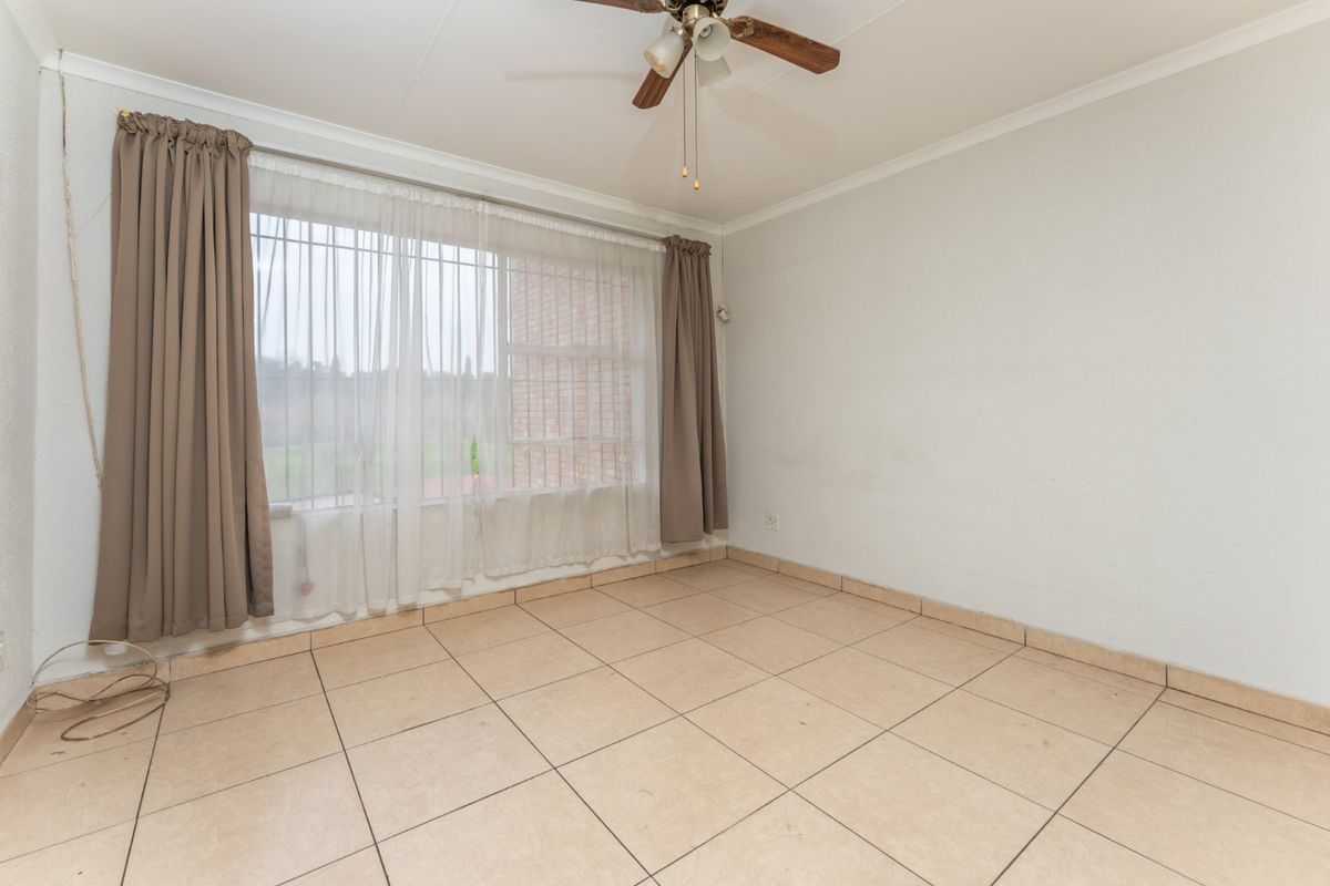 An empty bedroom featuring tiled flooring, a ceiling fan, and large windows fitted with security bars.