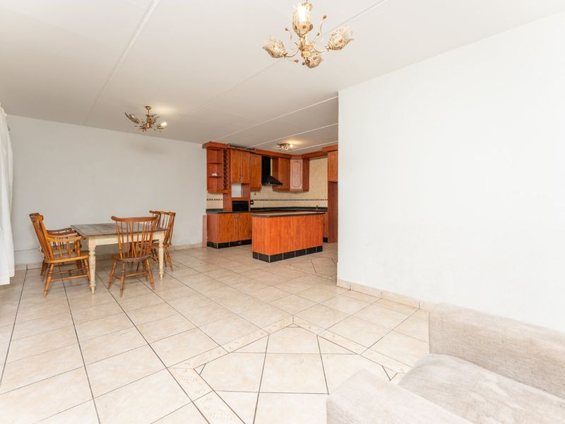 Open plan living and dining area featuring tiled flooring and a functional kitchen with wooden cabinetry and a central island.