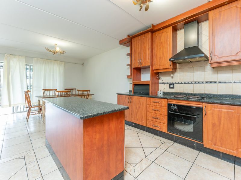 Open-plan kitchen and dining area featuring wooden cabinetry, granite countertops, built-in oven, and tiled flooring throughout.