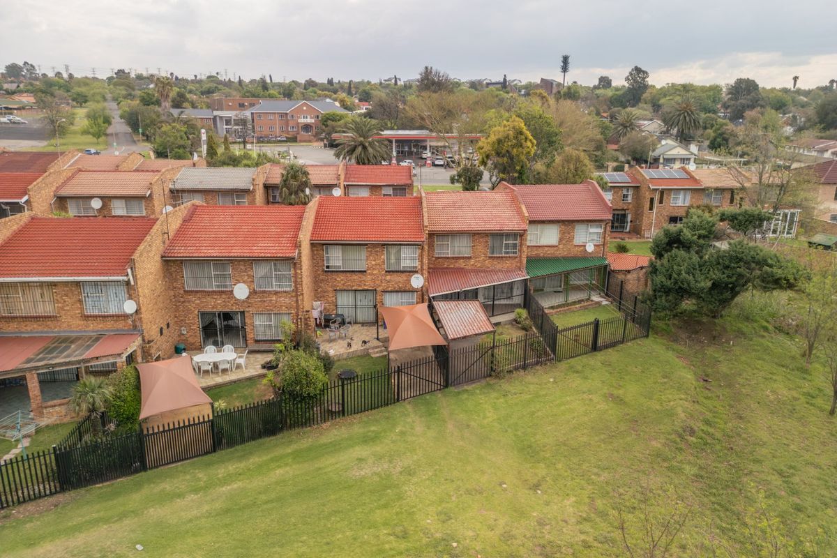 Aerial view of a townhouse complex featuring face brick exteriors, terracotta tiled roofs, private paved patios, and enclosed garden spaces.