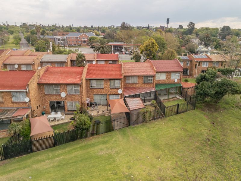 Aerial view of a townhouse complex featuring face brick exteriors, terracotta tiled roofs, private paved patios, and enclosed garden spaces.